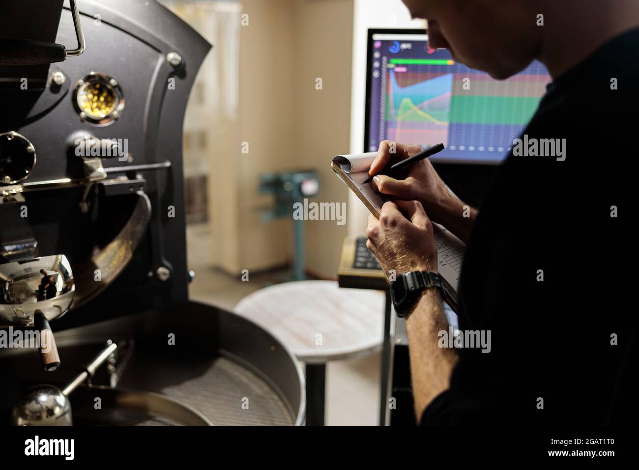 Un giovane lavoratore specializzato sta arrostendo il caffè nell'hangar Foto Stock
