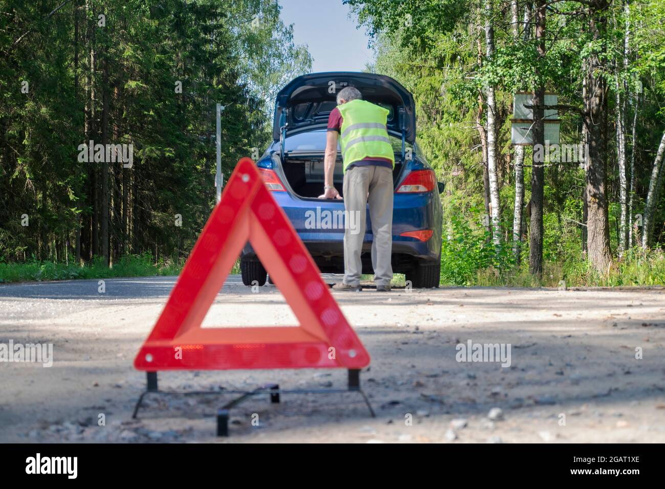 Il segnale di avvertenza rosso si trova sul lato della strada accanto al veicolo danneggiato Foto Stock