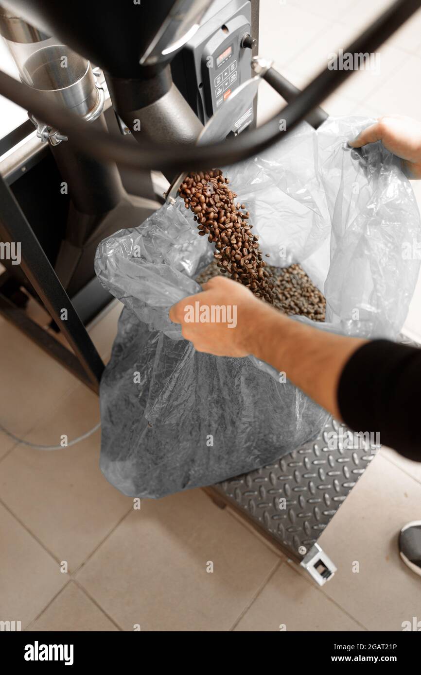 Un giovane lavoratore specializzato sta arrostendo il caffè nell'hangar Foto Stock