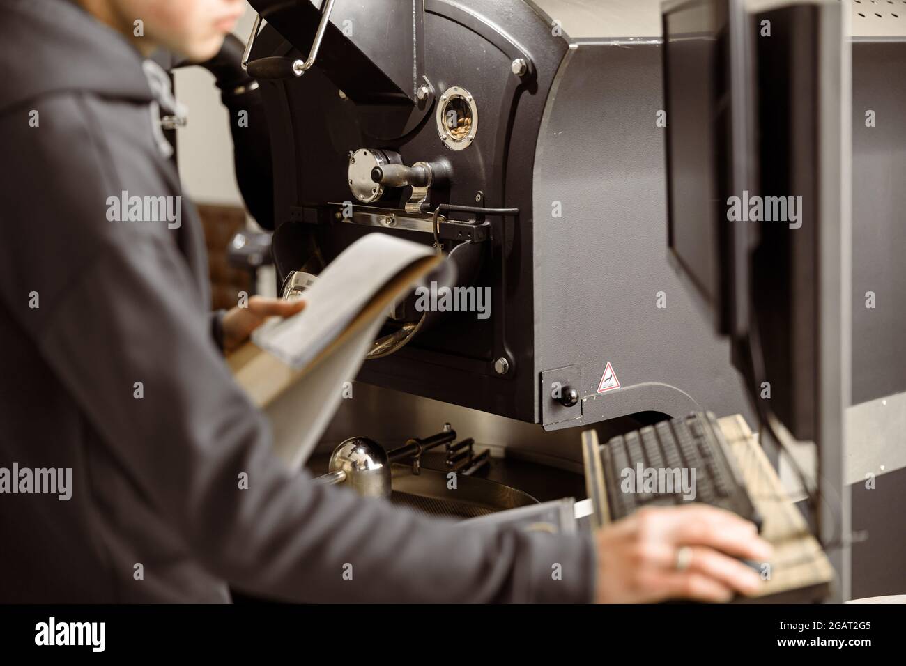 Un giovane lavoratore specializzato sta arrostendo il caffè nell'hangar Foto Stock