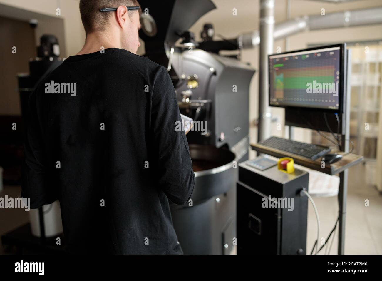 Un giovane lavoratore specializzato sta arrostendo il caffè nell'hangar Foto Stock