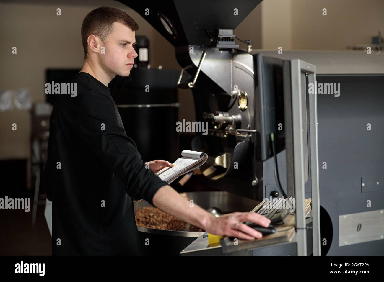 Un giovane lavoratore specializzato sta arrostendo il caffè nell'hangar Foto Stock