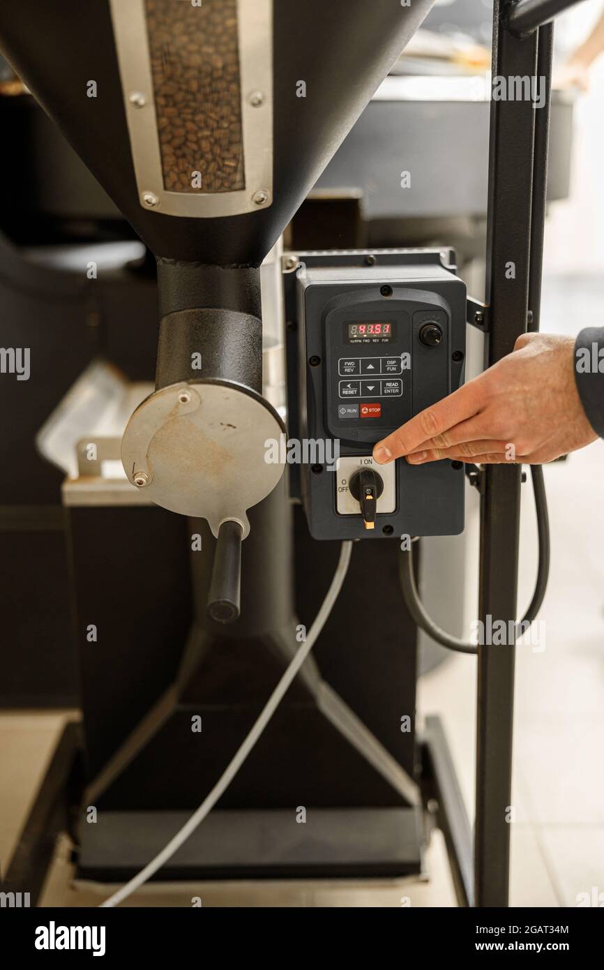 Un giovane lavoratore specializzato sta arrostendo il caffè nell'hangar Foto Stock