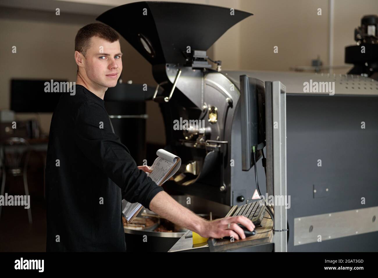 Un giovane lavoratore specializzato sta arrostendo il caffè nell'hangar Foto Stock