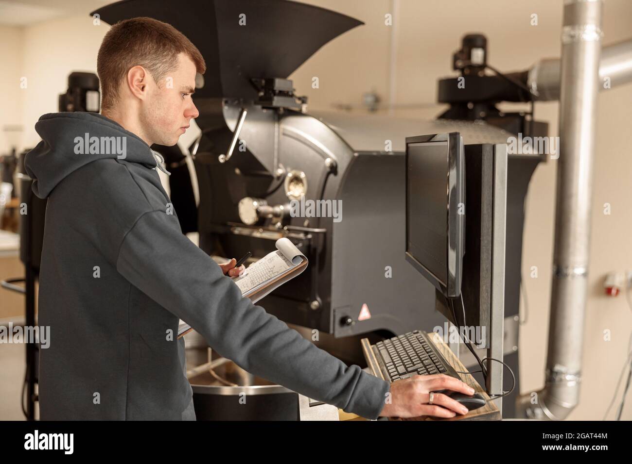 Un giovane lavoratore specializzato sta arrostendo il caffè nell'hangar Foto Stock