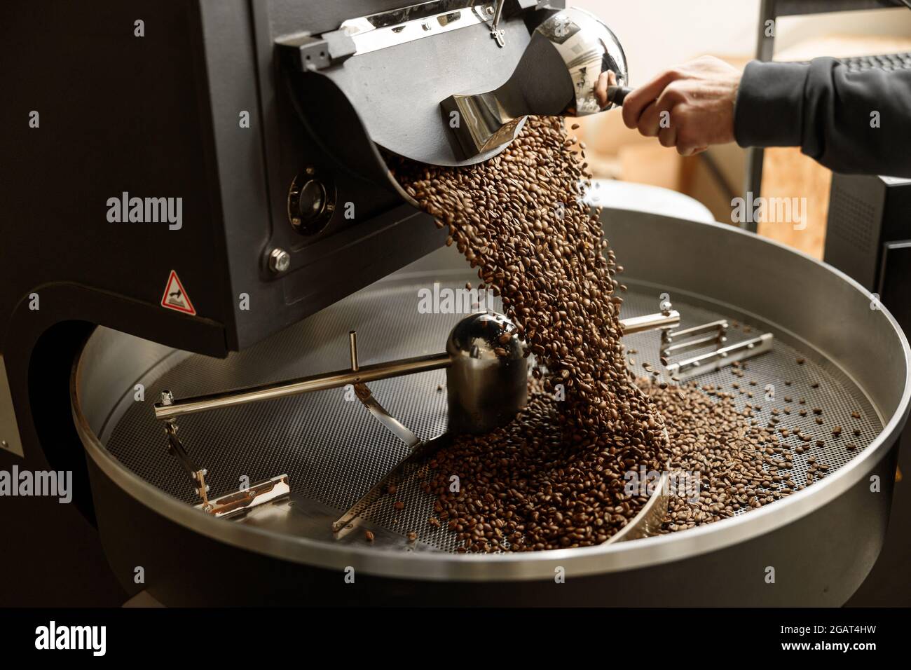Un giovane lavoratore specializzato sta arrostendo il caffè nell'hangar Foto Stock