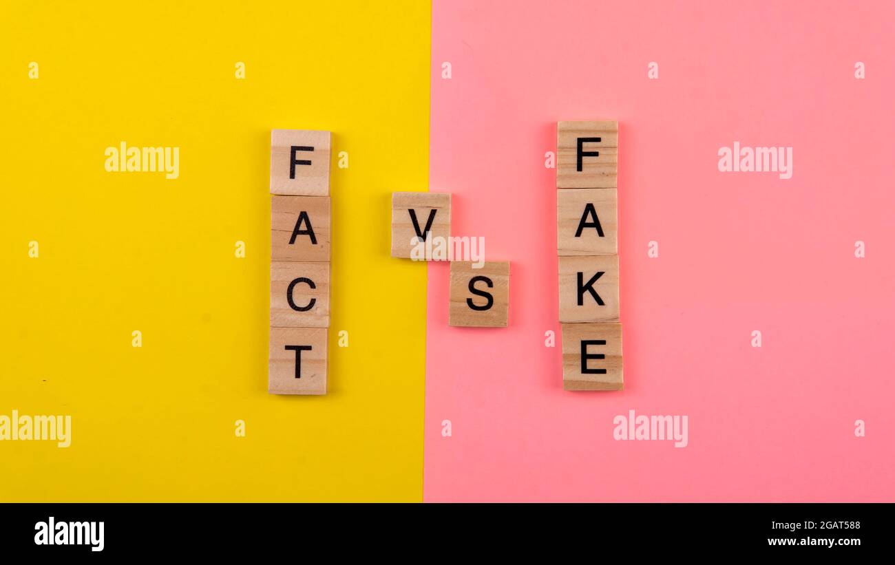 Un tessere di parola che forma il fatto di parola e falso su uno sfondo giallo e rosa. Fuoco selettivo sulla parola falso e sul fatto. Foto Stock