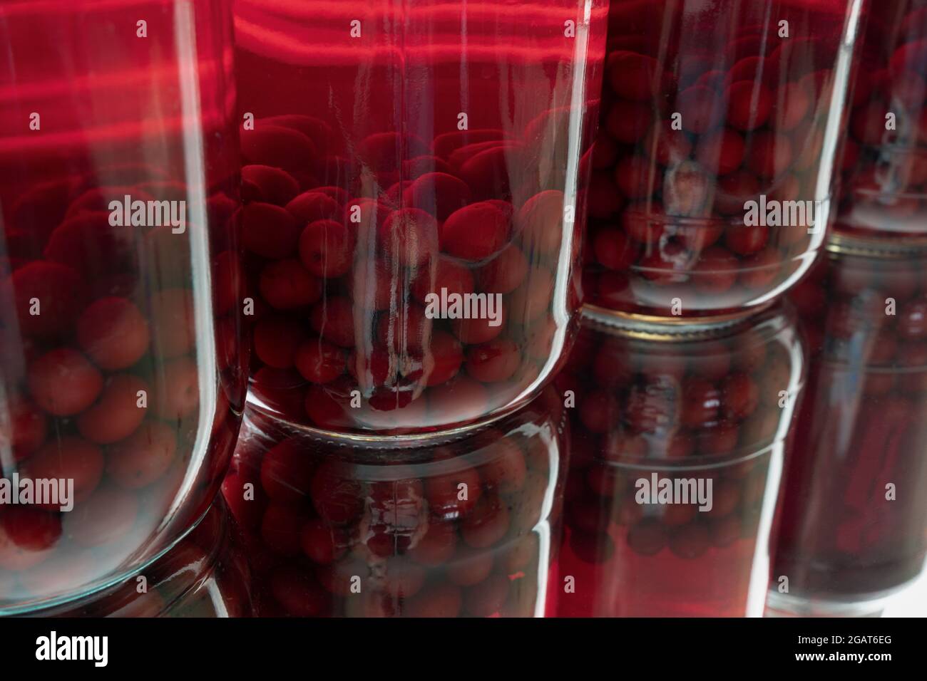 Giare di vetro a file con ciliegie rosse conservate in casa e i loro riflessi disposti diagonalmente Foto Stock