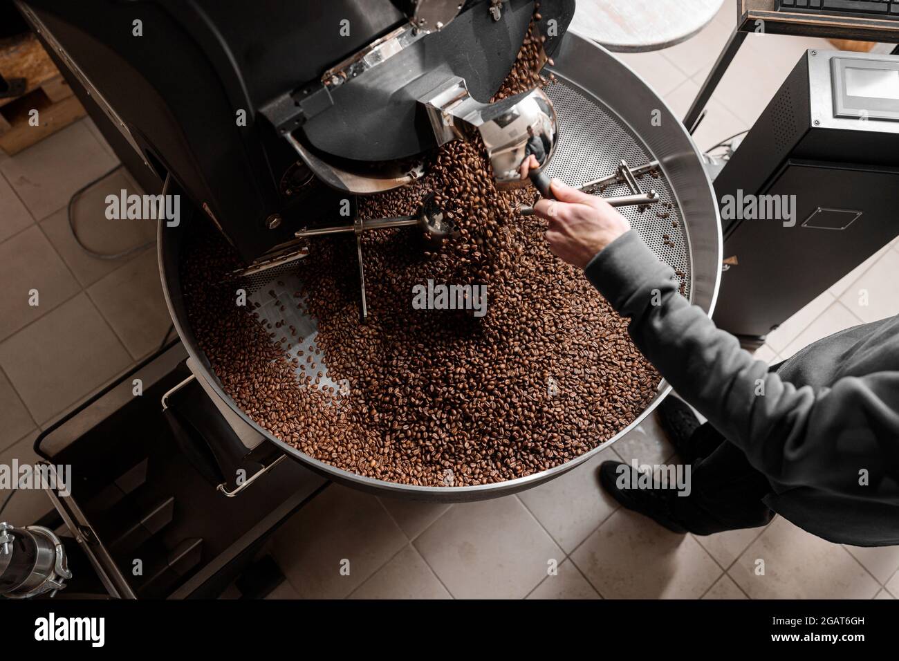 Un giovane lavoratore specializzato sta arrostendo il caffè nell'hangar Foto Stock