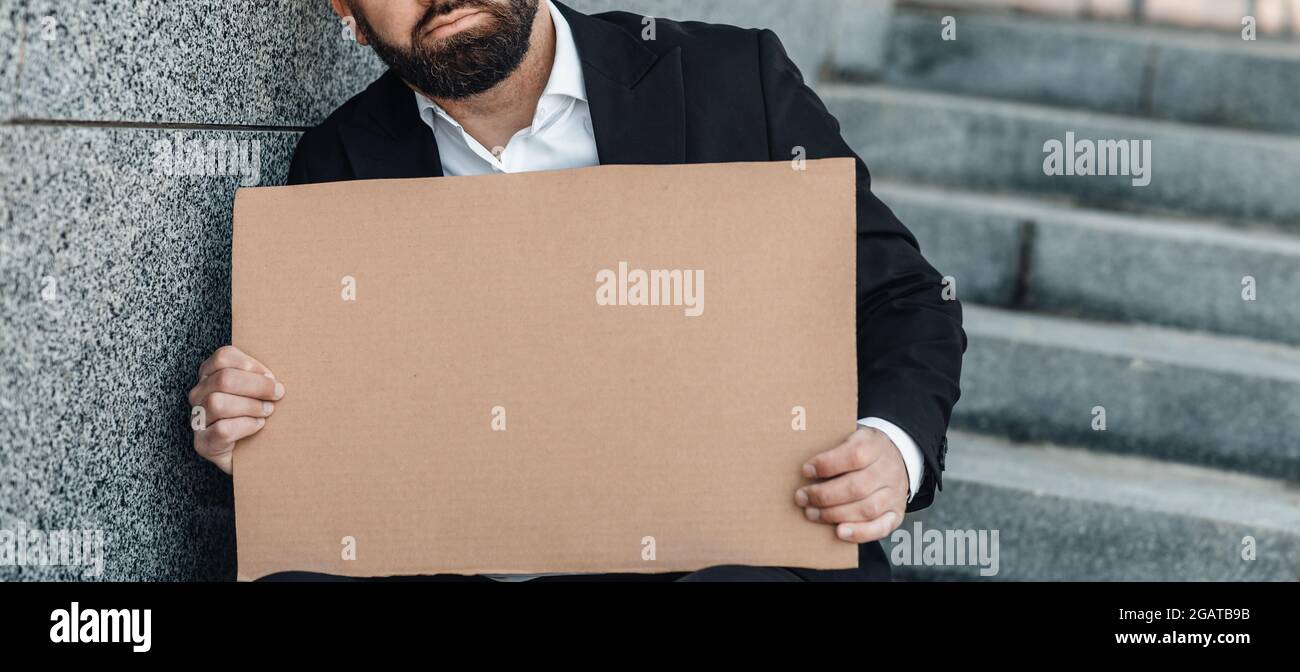 Concetto di ricerca del lavoro. Uomo d'affari irriconoscibile che tiene cartello di cartone vuoto, seduto all'aperto sulle scale, perso il lavoro e in cerca di lavoro, co Foto Stock