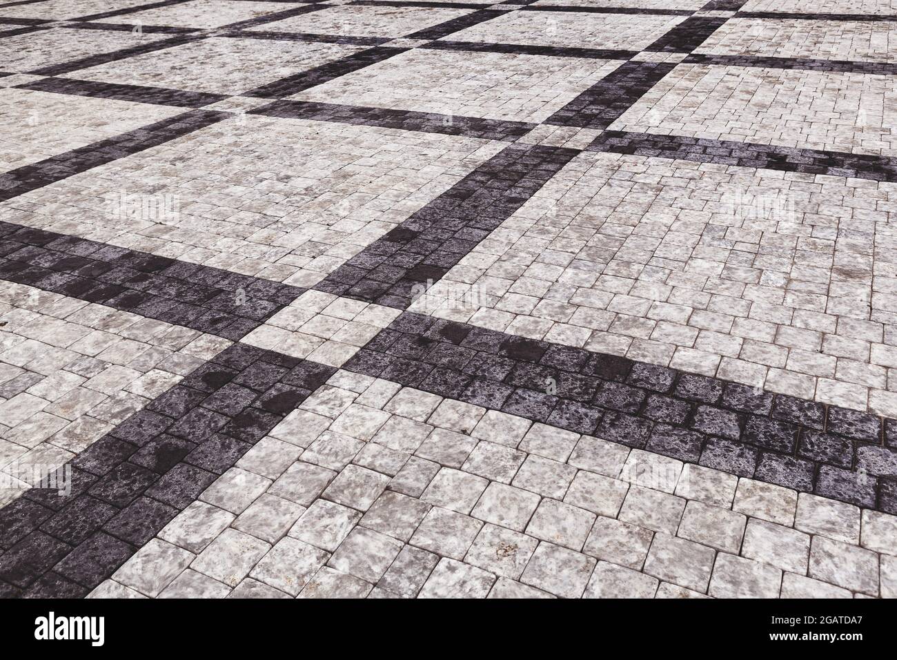 Marciapiede decorativo. Pavimento piastrellato con piastrelle grigie e nere, doppio-attraversato da una striscia diagonale di marmo vista ad angolo basso, full frame ba Foto Stock