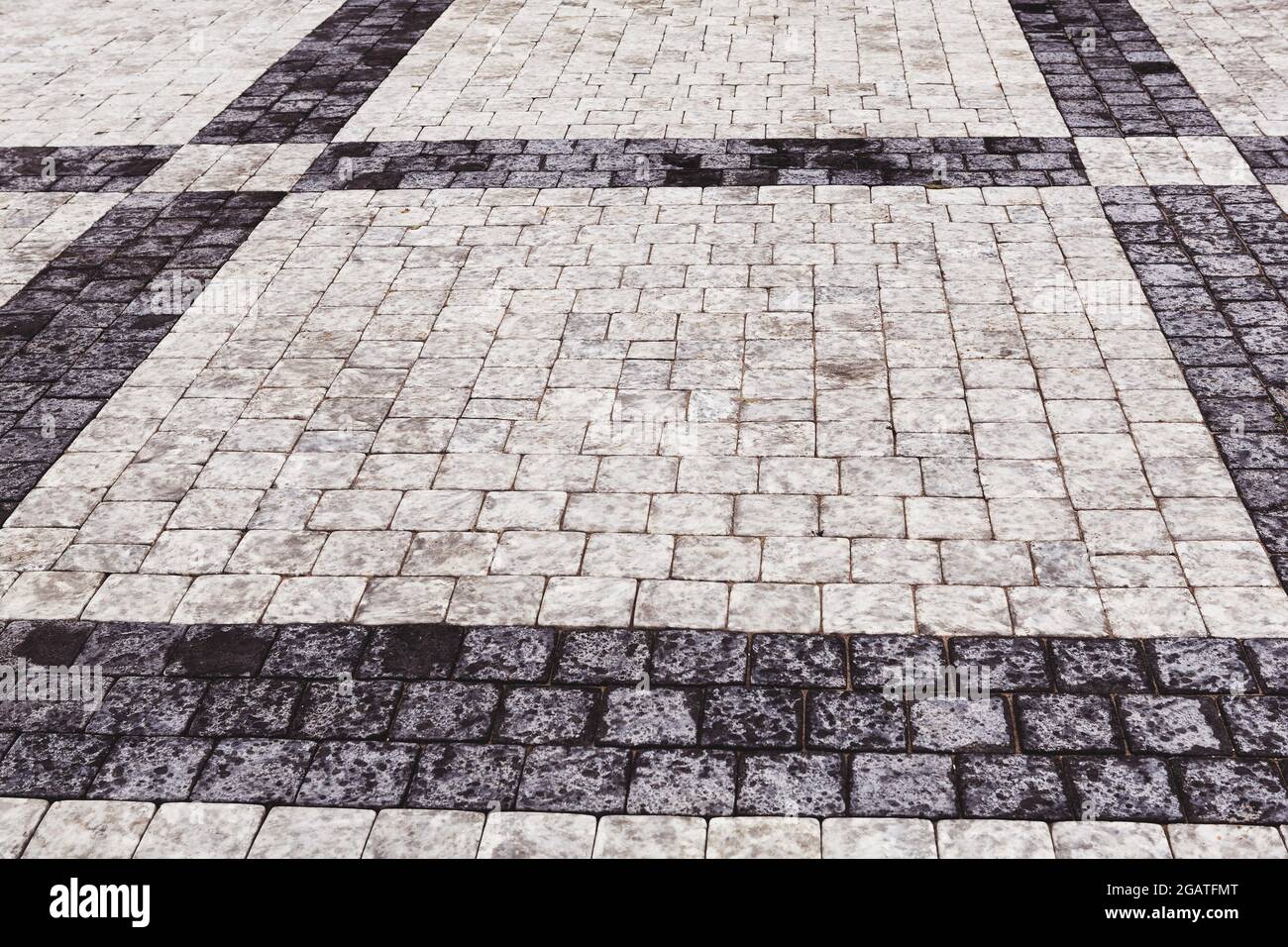 Marciapiede decorativo. Pavimento piastrellato con piastrelle grigie e nere, doppio-attraversato da una striscia diagonale di marmo vista ad angolo basso, full frame ba Foto Stock