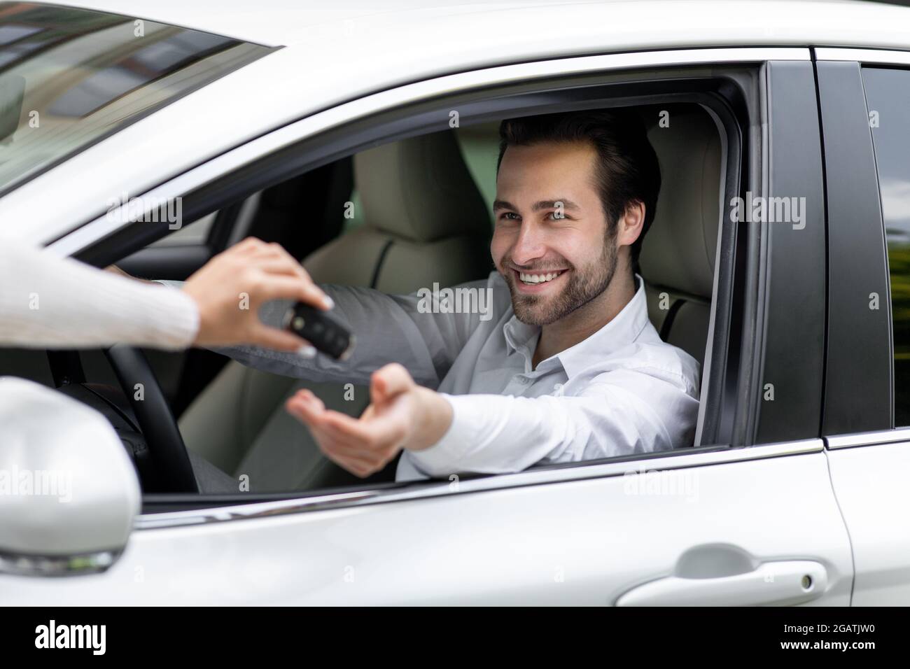 La mano più in alto femmina dà la chiave dell'automobile alla mano maschio nella concessionaria. Industria automobilistica, assicurazione o commercio di automobile. Giovane sorridente bel ragazzo caucasico dentro Foto Stock