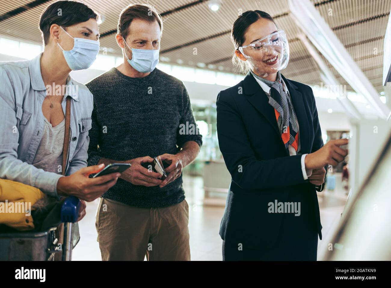 Il personale dell'aeroporto aiuta la famiglia con il check-in self-service durante la pandemia. Famiglia di passeggeri aiutata da compagnie aeree in aeroporto in pandemia. Foto Stock