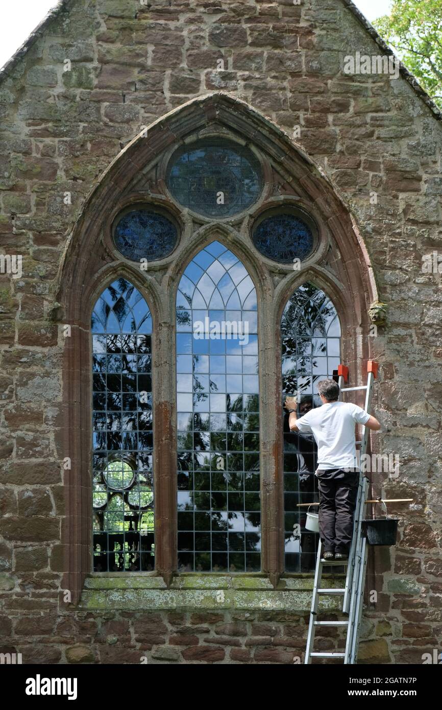 Un pulitore volontario della finestra sale una scala per pulire il vetro esterno della finestra est di Mary's Church, Longnor, Shropshire, Inghilterra, Regno Unito Foto Stock