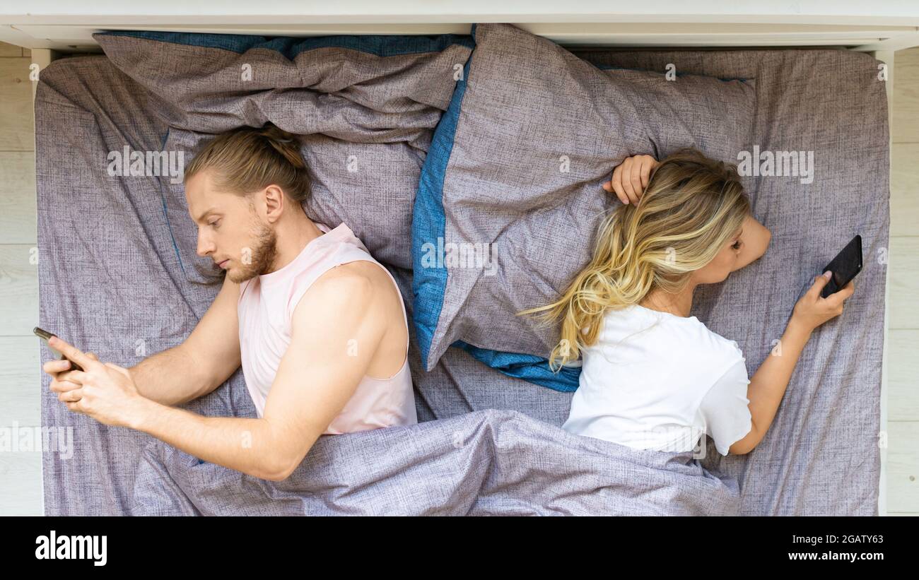 Concetto di dipendenza dal telefono cellulare - vista dall'alto di una coppia a letto con telefoni cellulari. Navigano in Internet senza essere interessati l'uno all'altro. Foto Stock