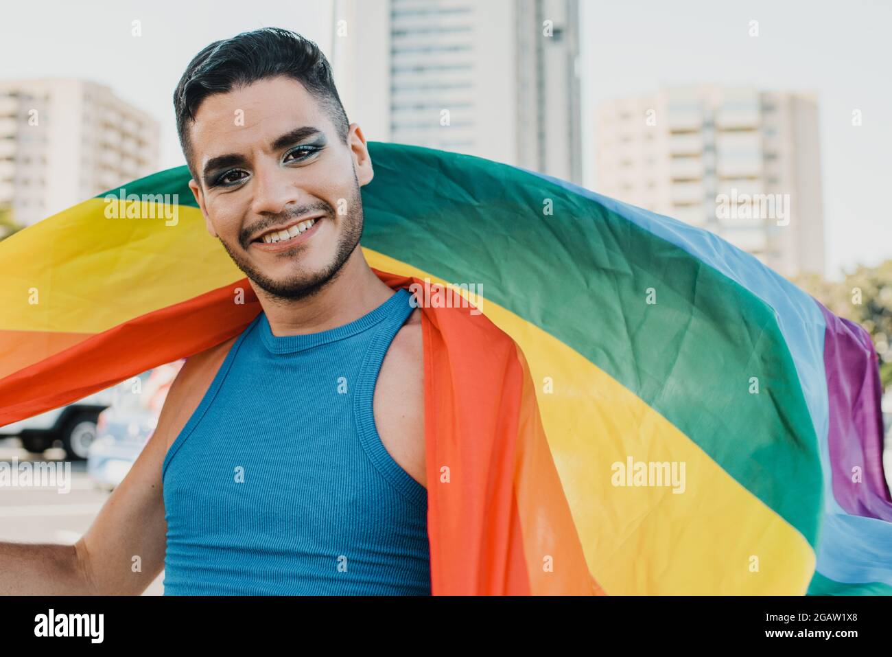 Giovane uomo gay ispanico che indossa bandiera multicolore in strada sensazione di felicità Foto Stock