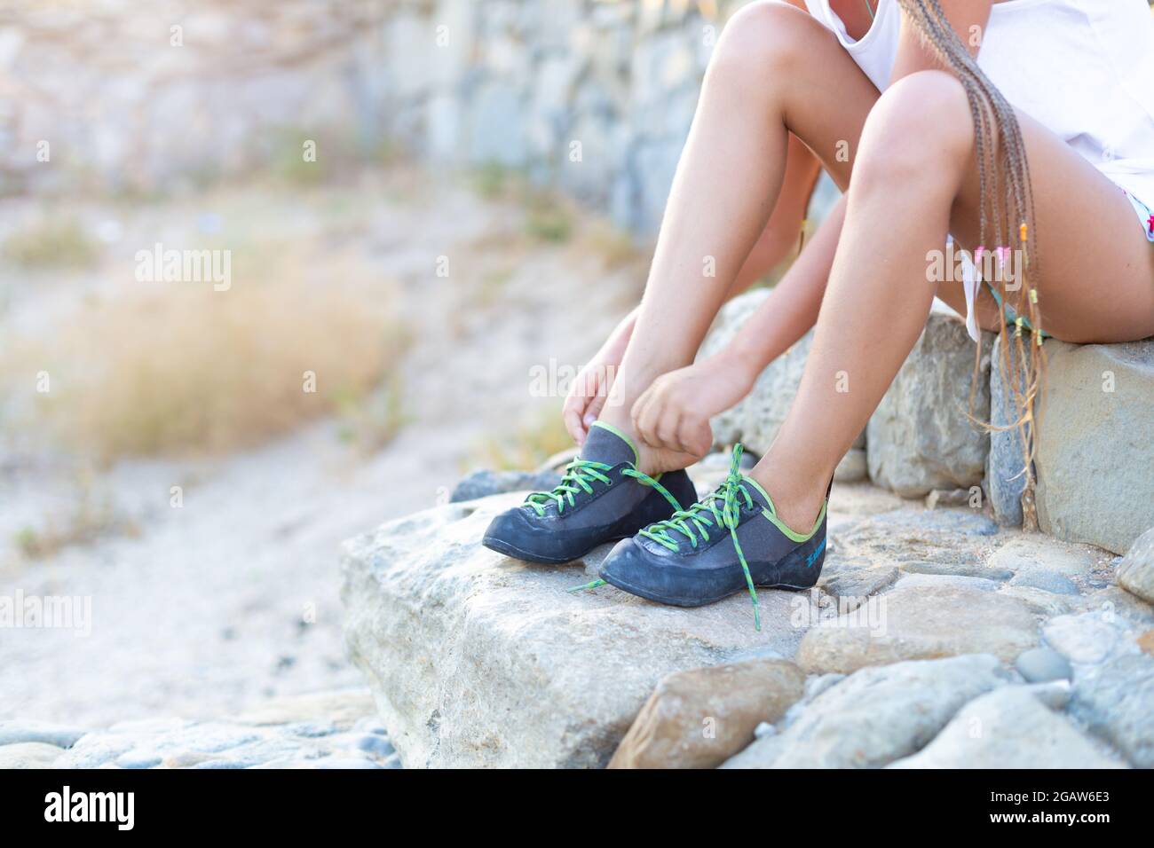 Un bambino indossa scarpe da arrampicata mentre si siede sui gradini di pietra. Una ragazza si sta preparando per una sessione di arrampicata in aria aperta. Un piede Foto Stock