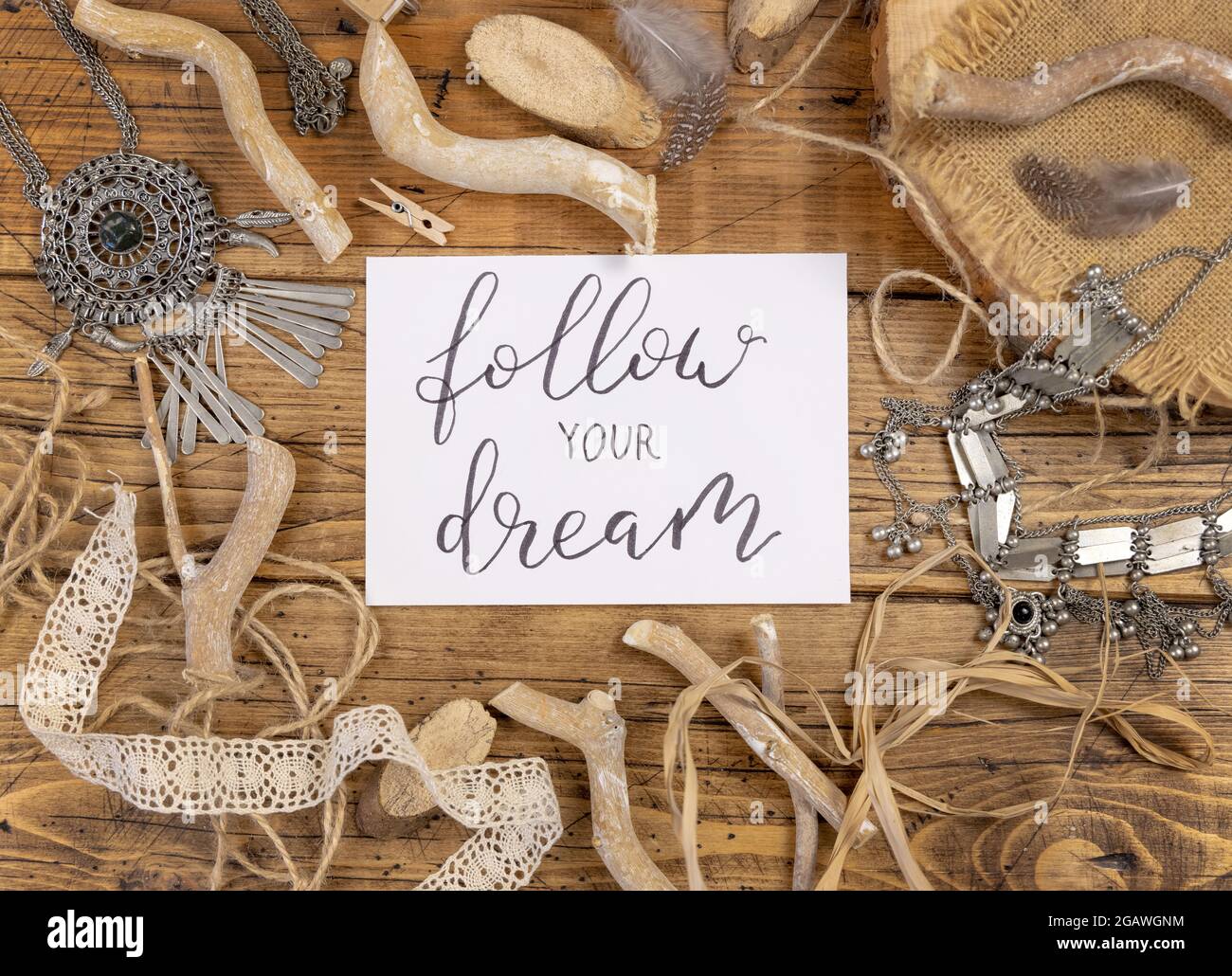 Scheda con il testo scritto a mano SEGUI IL TUO SOGNO con decorazioni bohémien intorno vista dall'alto su un tavolo di legno Foto Stock