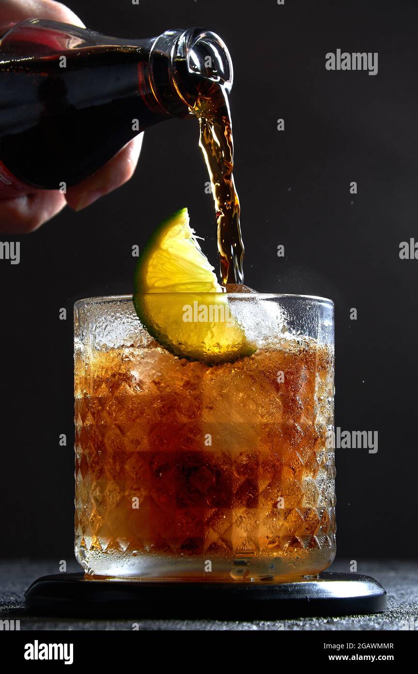 Cuba Libre o Long Island cocktail con cola, rum e lime in vetro su sfondo scuro. Rinfrescante bevanda estiva. Foto Stock