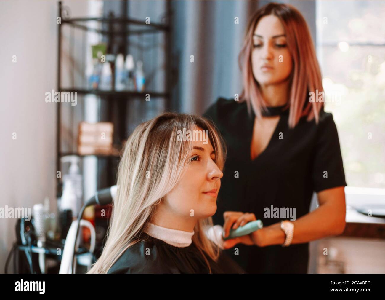 Donna felice con stilista che fa i capelli al salone. Competente donna parrucchiere decidere cosa fare in parrucchiere con brunette femmina cliente. Due beaut Foto Stock