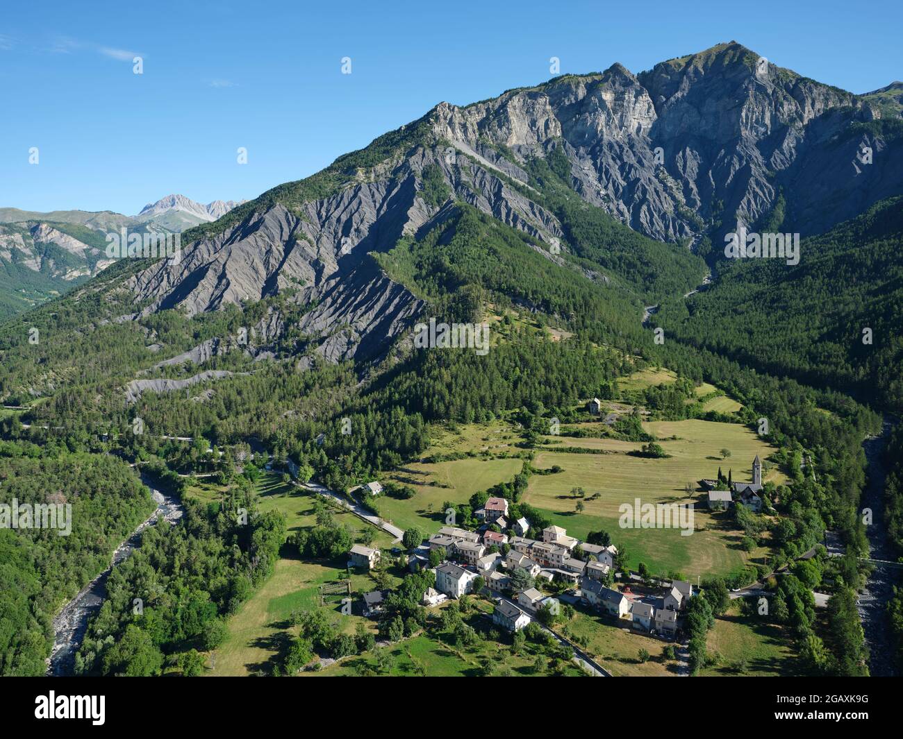 VISTA AEREA. Villaggio di Villeneuve d'Entraunes ai piedi di una montagna rocciosa nella Valle del Var superiore. Alpi Marittime, Francia. Foto Stock