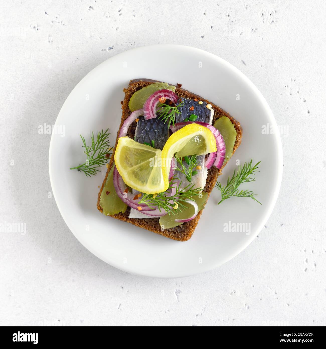 Sandwich con pesce di aringa e cetrioli di sottaceti su piatto bianco. Vista dall'alto, disposizione piatta Foto Stock