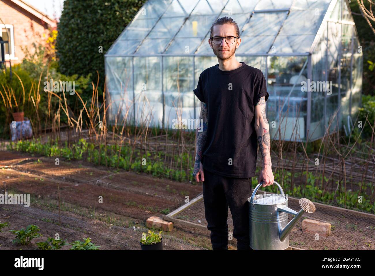 Woodbridge Suffolk UK Maggio 08 2020: Un giovane hipster maschile tatuato che lavora con orgoglio nel suo orto coltivando una gamma di verdure biologiche Foto Stock