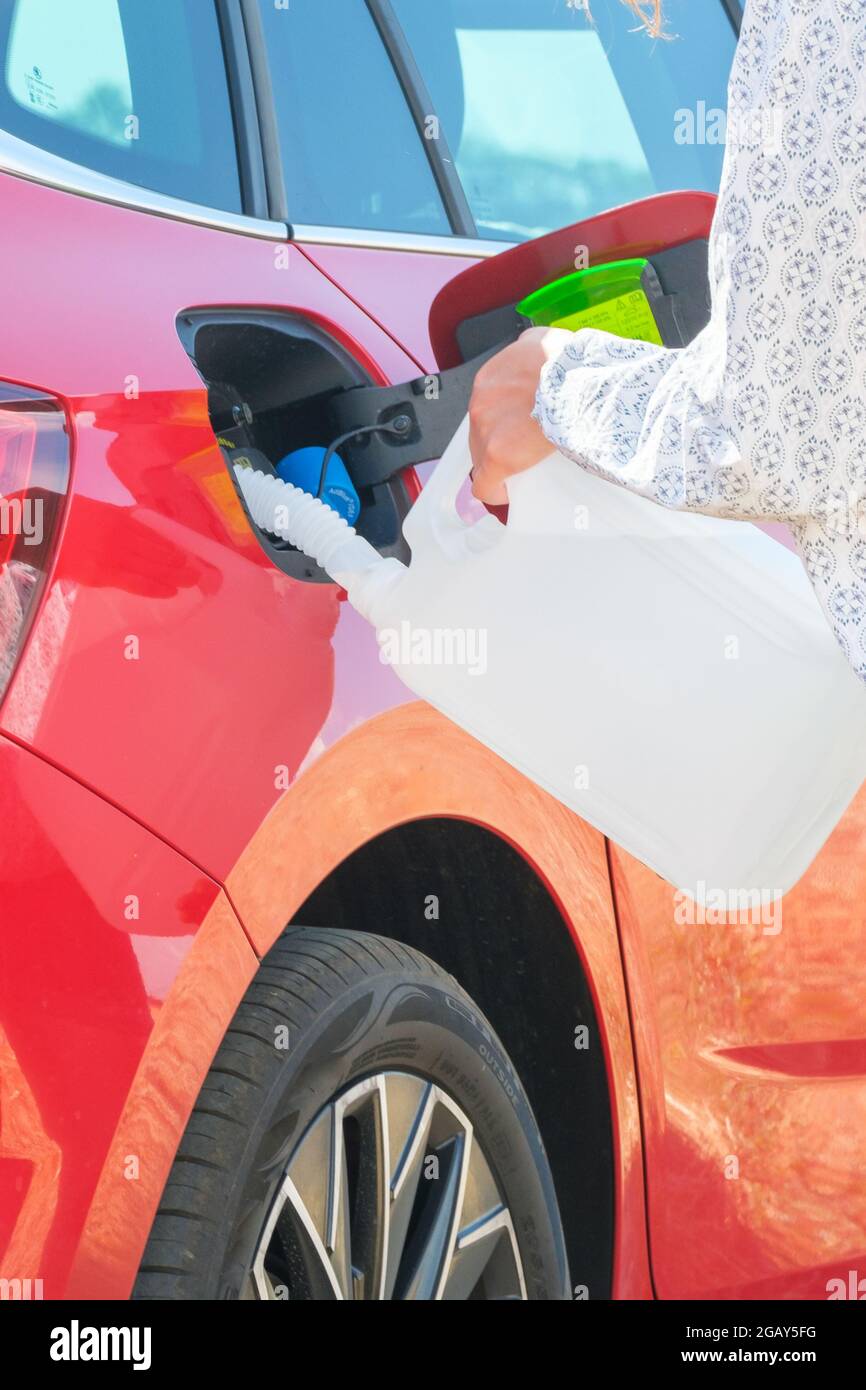 Donna che riempie un liquido motore diesel dal barattolo nel serbatoio dell'auto rossa sullo sfondo delle turbine eoliche. Riduzione dell'inquinamento atmosferico e. Foto Stock