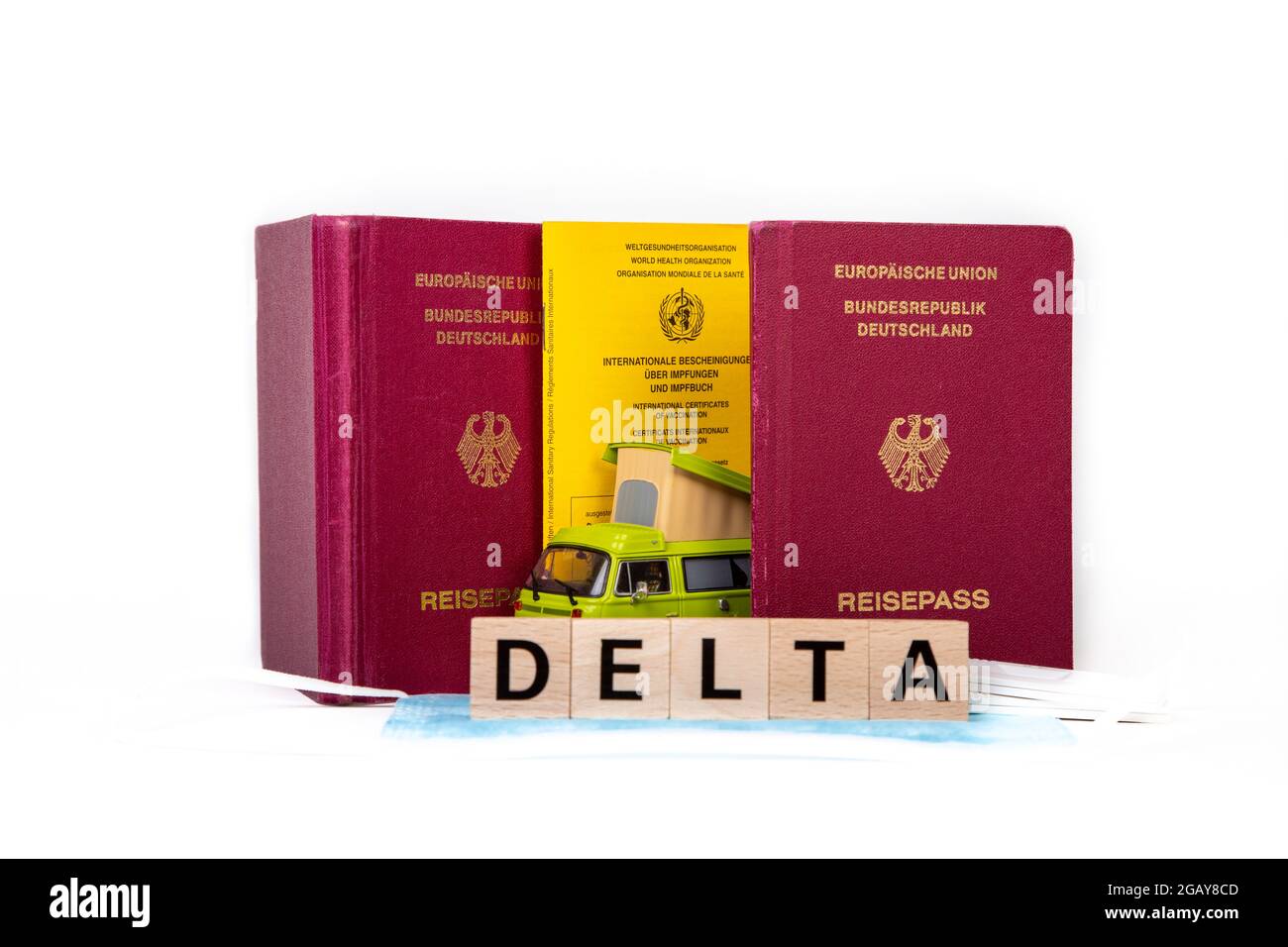 Huerth, NRW, Germania, 08 01 2021, passaporto tedesco e libro vaccino, blocco di legno con la parola DELTA, una maschera facciale e un camper giocattolo auto Foto Stock