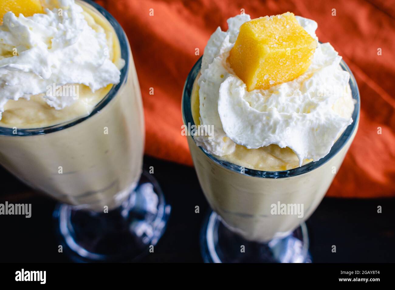 Frullati di cocco Mango serviti in bicchieri Fountain: Bevande surgelate frullate a base di mango e latte di cocco e guarnite con panna montata Foto Stock