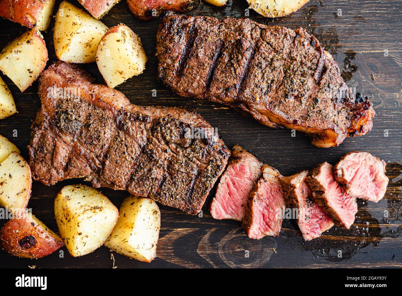 NY Strip Steak alla griglia con Coffee Rub e patate arrosto: Bistecche alla griglia di New York Strip con patate arrostite su sfondo di legno scuro Foto Stock