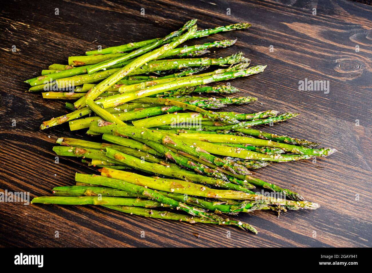 Asparagi arrosto su sfondo di legno scuro: Asparagi arrosto conditi con olio extra vergine di oliva, sale kosher e pepe nero Foto Stock