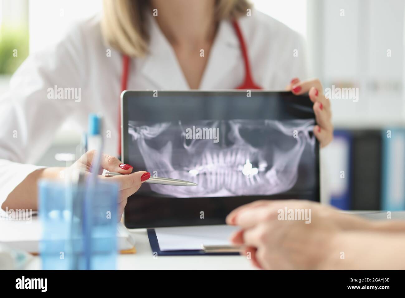 Il dentista professionista mostra i raggi X delle mascelle e dei denti del paziente utilizzando un tablet digitale Foto Stock