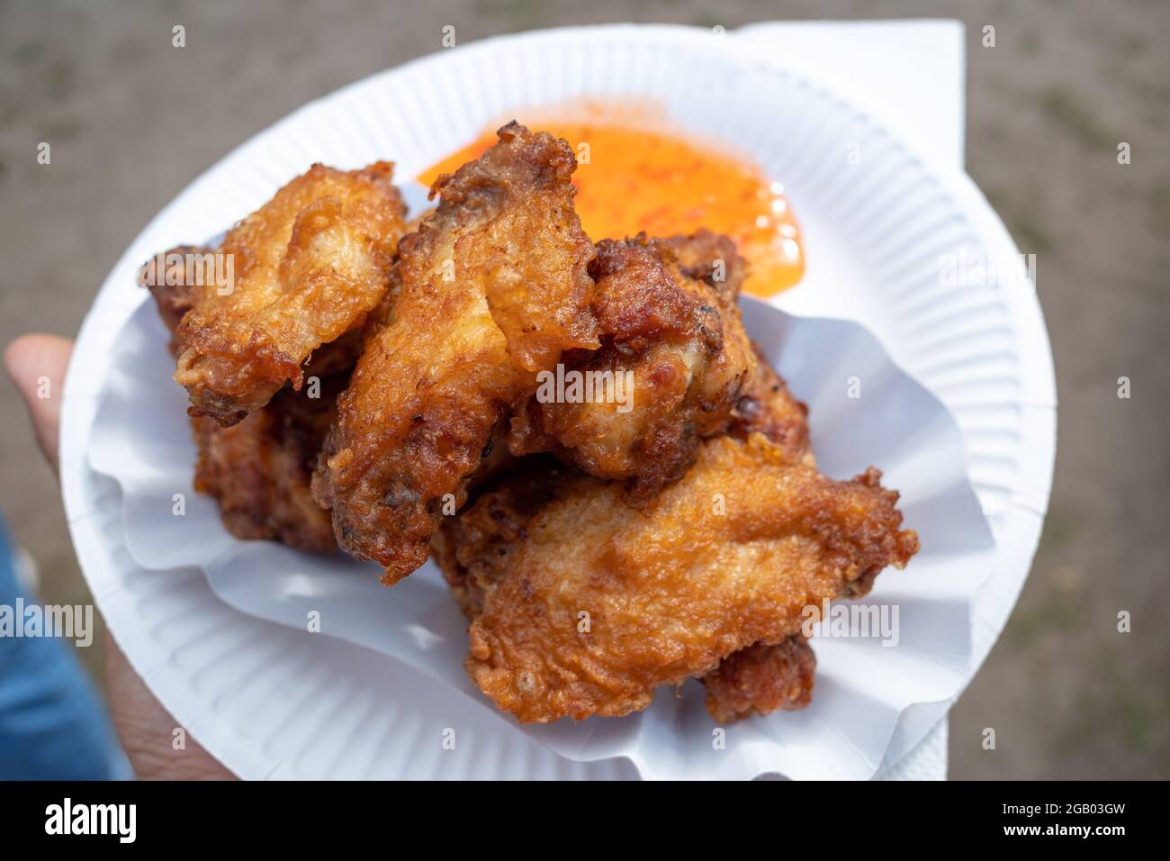 Tenere a mano il pollo fritto in stile asiatico e la salsa piccante dolce e aspre su un piatto di carta bianca. Foto Stock