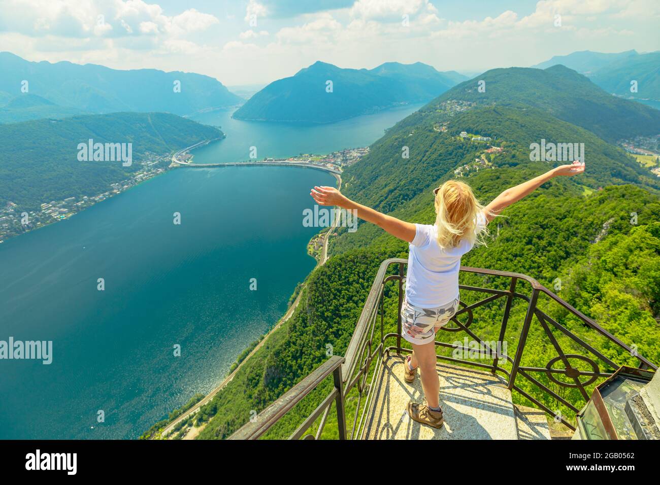 Donna svizzera a braccia aperte sul monte San Salvatore sul lago di Lugano in Svizzera. Veduta aerea di Lugano con nel Cantone Ticino. Foto Stock