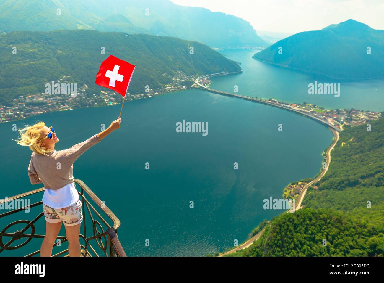 Ragazza con bandiera svizzera in cima allo skyline di Lugano dalla vetta di San Salvatore nel Cantone Ticino. Lago di Lugano in Svizzera. Vista aerea da San Foto Stock