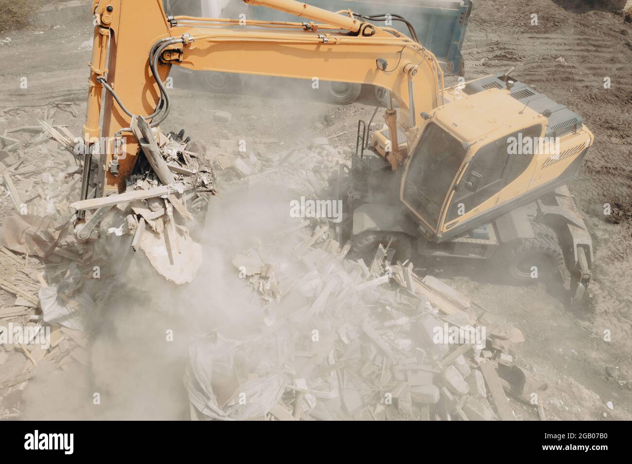 L'escavatore rompe gli edifici e carica i rifiuti di costruzione nel dumper con la sua benna. Demolizione di edifici. Foto Stock