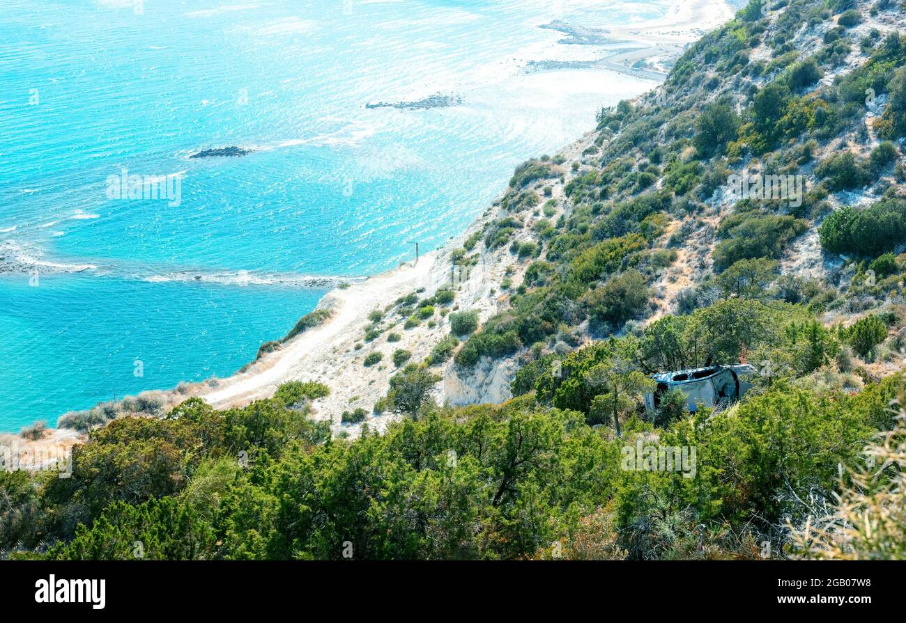 L'auto si è schiantata cadde da una scogliera a una riva. Scenario di incidente in idilliaco paesaggio mediterraneo con spiaggia di mare Foto Stock