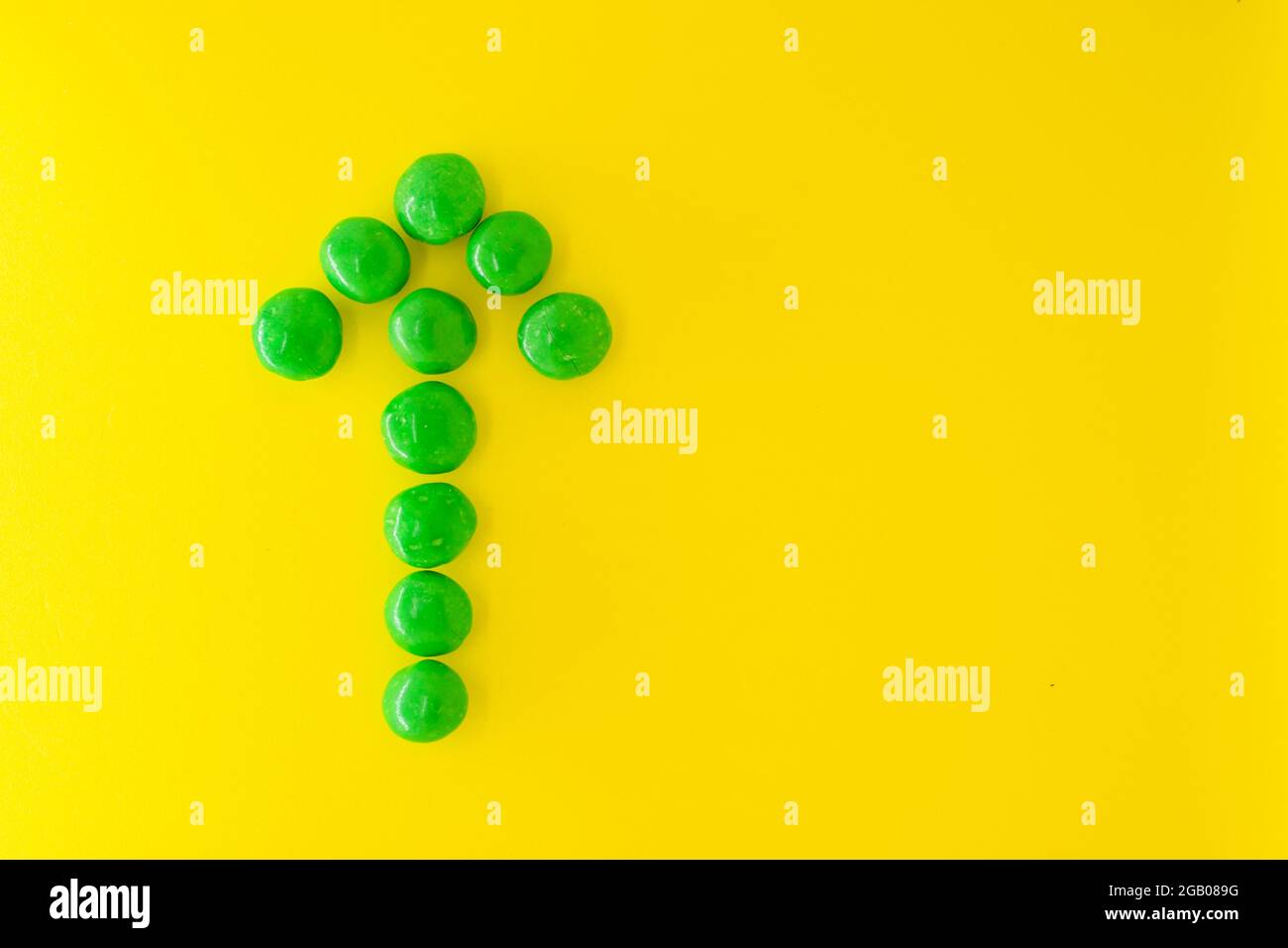 Freccia verde del puntatore della caramella al cioccolato su sfondo giallo con spazio di copia per il testo, piatto. Foto Stock