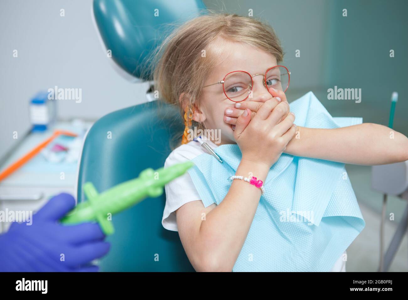 La bambina spaventa rifiutandosi di aprire la bocca per il dentista con una siringa, coprendo la bocca con le mani Foto Stock
