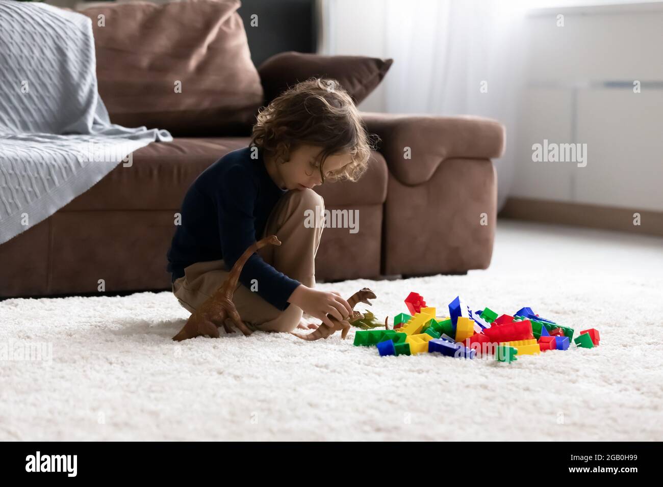 Piccolo ragazzo carino concentrato seduto sul pavimento a casa Foto Stock