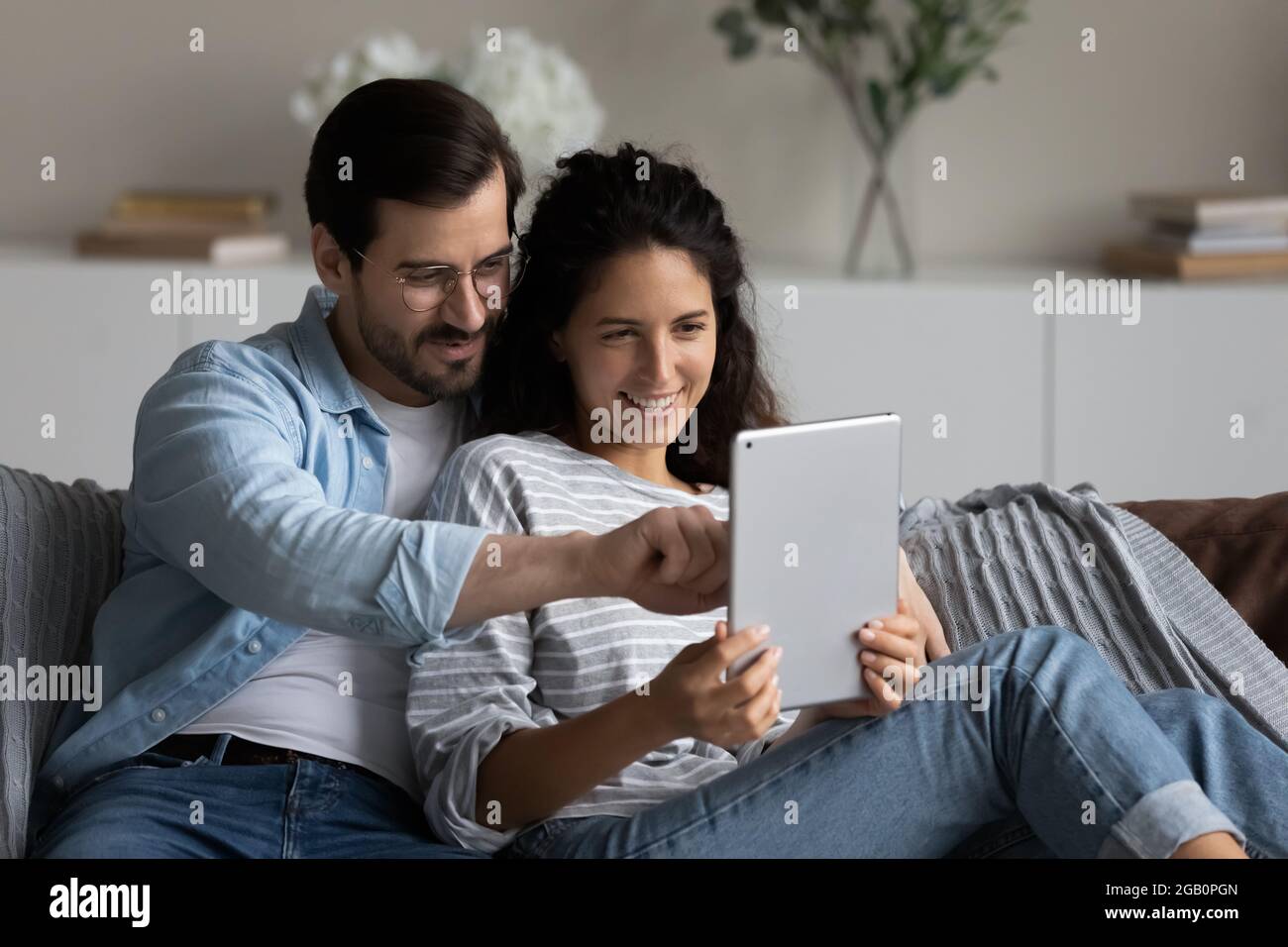 Felice rilassata coppia millennial con tablet hugging sul divano Foto Stock