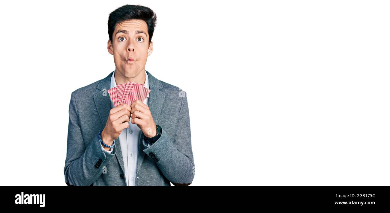 Giovane uomo d'affari ispanico che copre faccia con le schede che fanno faccia del pesce con la bocca e gli occhi squinting, pazzo e comico. Foto Stock