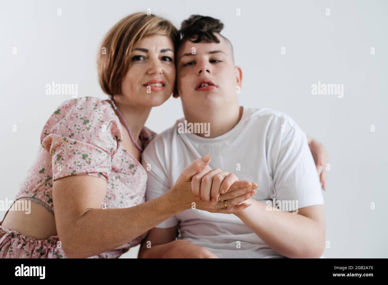 Madre abbracciando disabile ragazzo 17 anni in sedia a rotelle con paralisi cerebrale su sfondo bianco. Donna assiste la persona con bisogni speciali. Emotivo Foto Stock