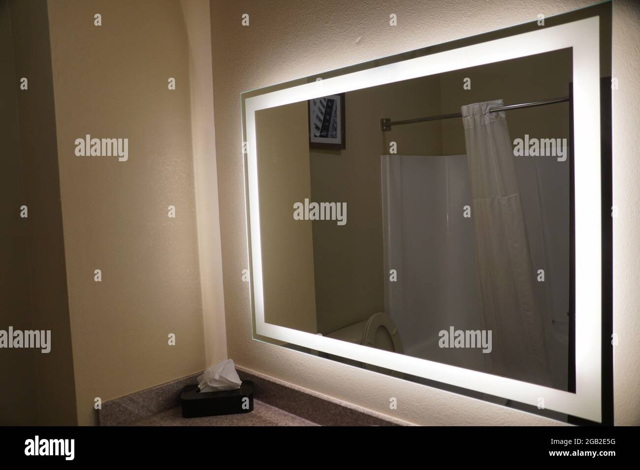 Un grande specchio da bagno con luci illuminate sui bordi Foto Stock