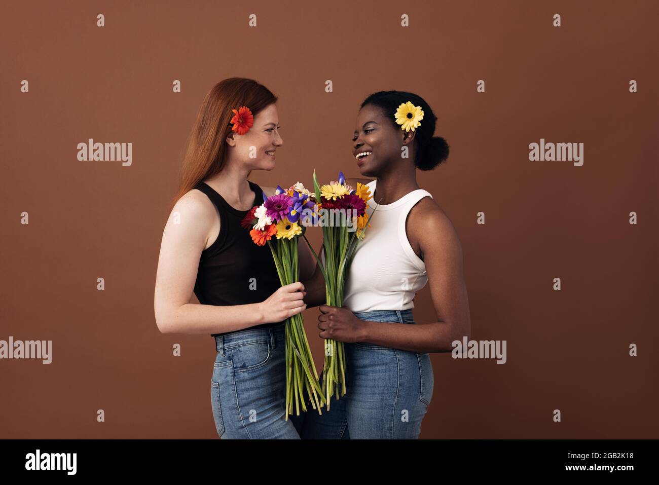 Due donne di razze diverse che tengono mazzi di fiori che si guardano l'un l'altro in uno studio Foto Stock