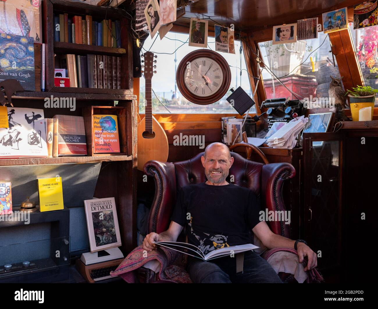 Word on Water, una libreria situata su una chiatta ormeggiata permanentemente a King's Cross, Londra. L'uomo seduto è Giovanni, il co-proprietario. Foto Stock