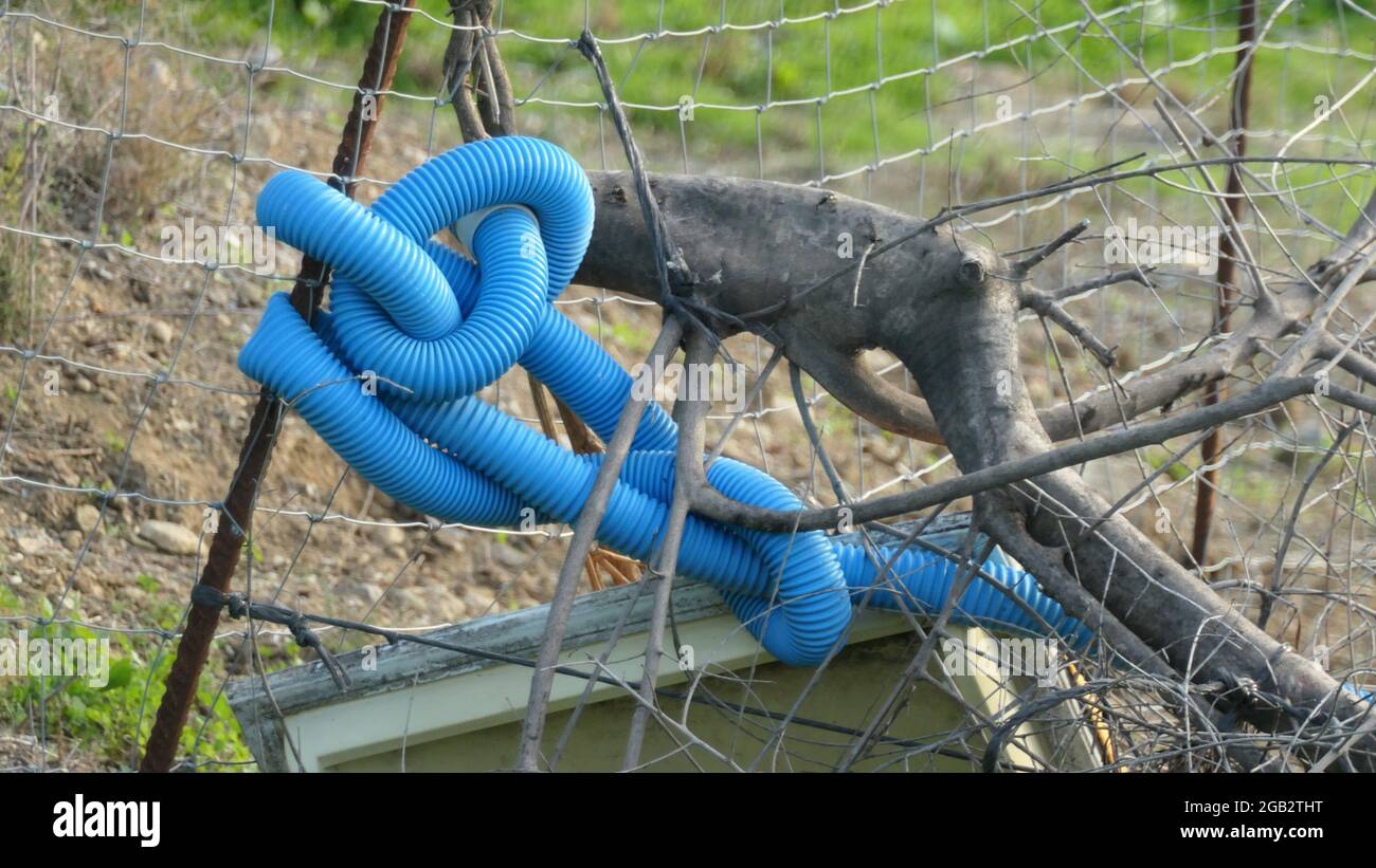 Tubo protettivo in plastica blu legato in nodi intorno al montante di recinzione Foto Stock