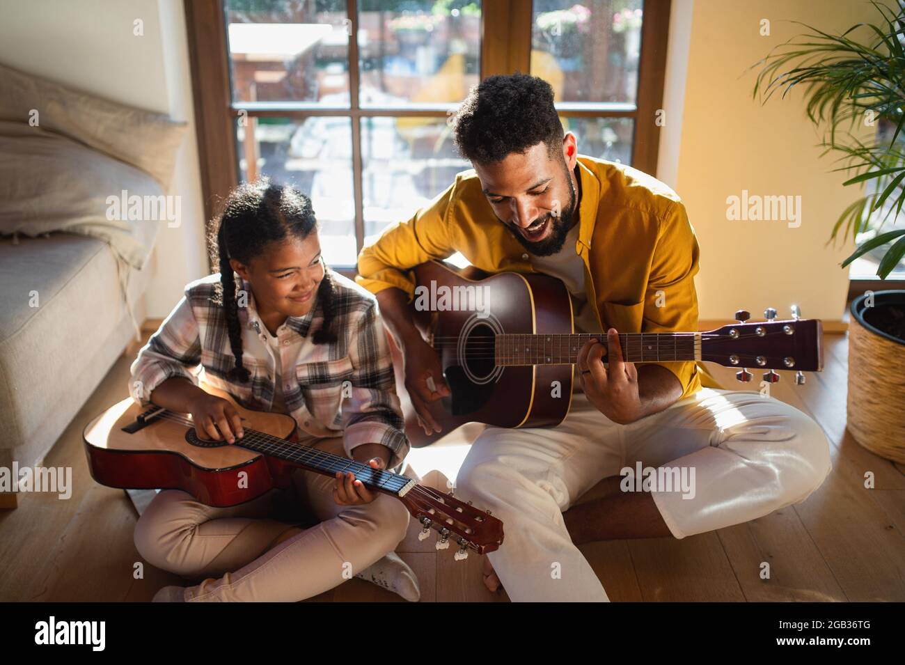 Vista ad alto angolo del padre felice con la piccola figlia al chiuso a casa, suonando la chitarra. Foto Stock